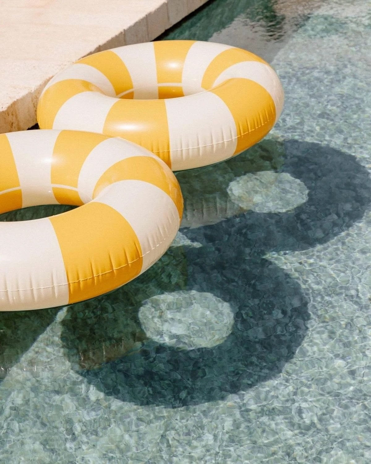Placeholder photo: two yellow and cream striped pool floats on clear water